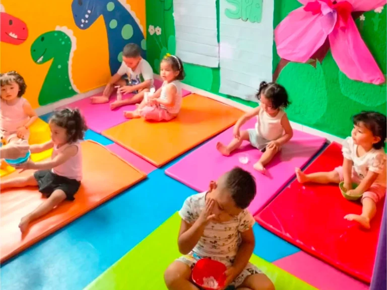 Niños jugando sobre colchonetas en una sala colorida con paredes decoradas.