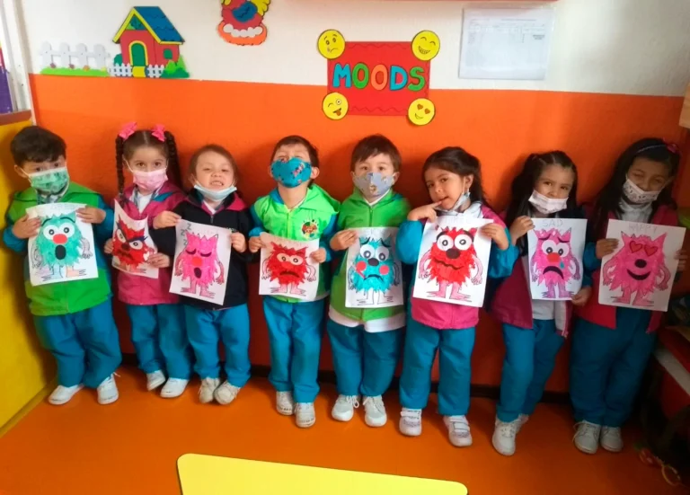 Niños en uniforme escolar mostrando dibujos de monstruos coloridos.