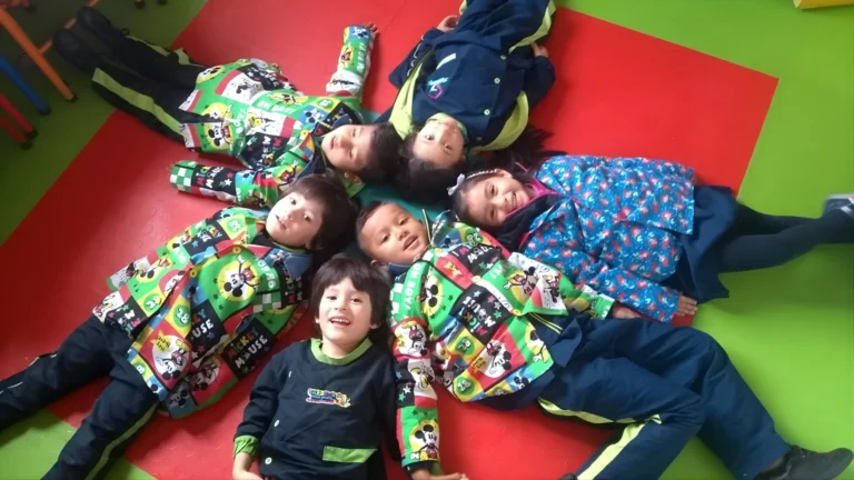 Niños sonrientes recostados en el suelo con coloridos uniformes escolares.