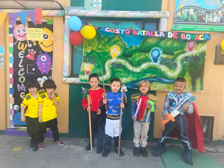 Niños disfrazados de personajes históricos y superhéroes frente a una decoración colorida.