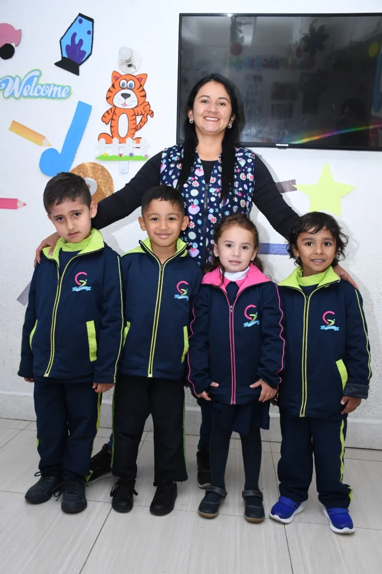Mujer con niños en uniforme escolar frente a pared decorada.