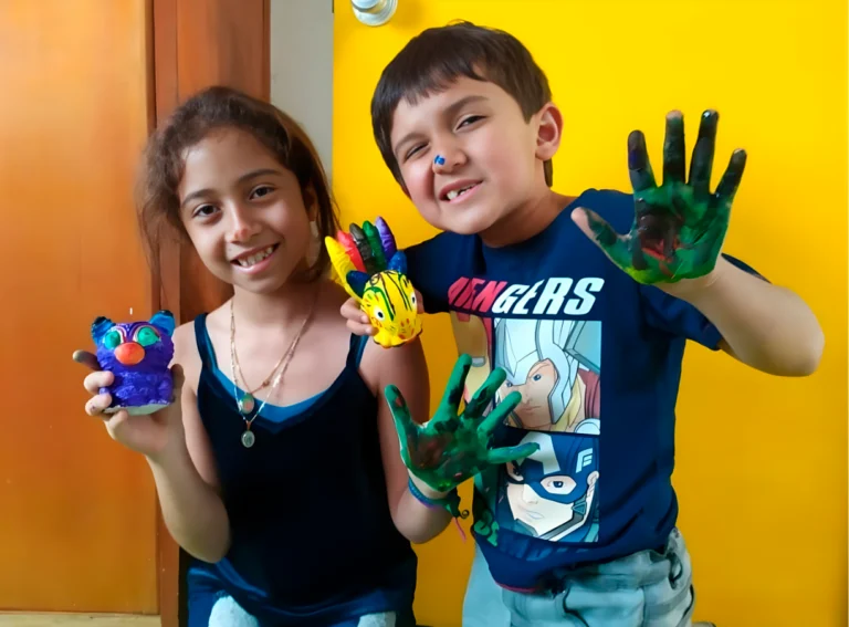 Niños sonrientes muestran manos pintadas y figuras coloridas.