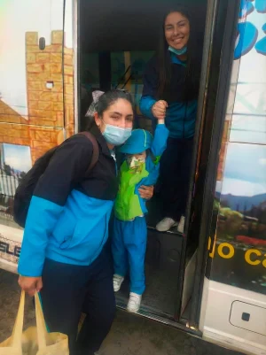 Mujer y niño con uniforme escolar azul y verde bajan de un autobús.